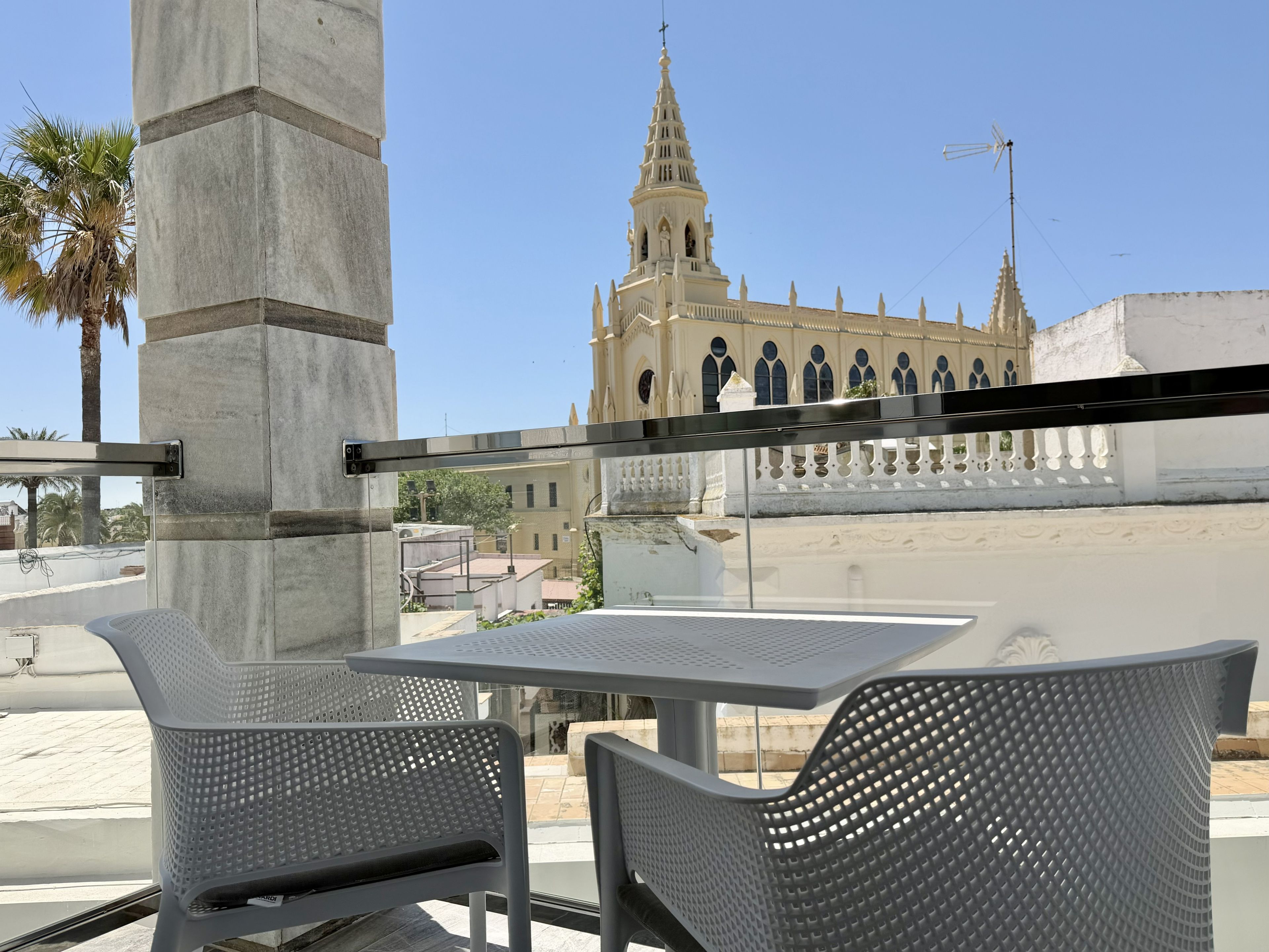 Un área de estar al aire libre con dos sillas y una mesa, con vista a un edificio histórico con una torre alta.