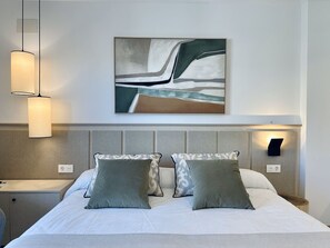 A hotel room with a bed, two bedside lamps, a headboard, and a wall-mounted abstract painting. - Hotel Apartamentos Marina Luz (Chipiona)