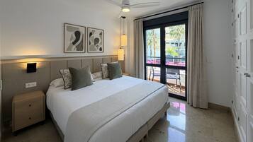 A hotel room with a bed, bedside tables, a ceiling fan, a window with curtains, and artwork on the wall.