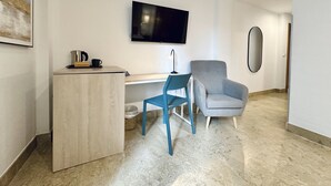 A modern hotel room with a wooden desk, a blue chair, a grey armchair, a flat-screen TV, and a large mirror. - Hotel Apartamentos Marina Luz (Chipiona)