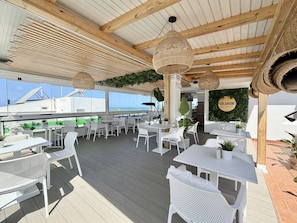 An outdoor dining area with white wicker furniture, hanging wicker lamps, and a view of the sea.