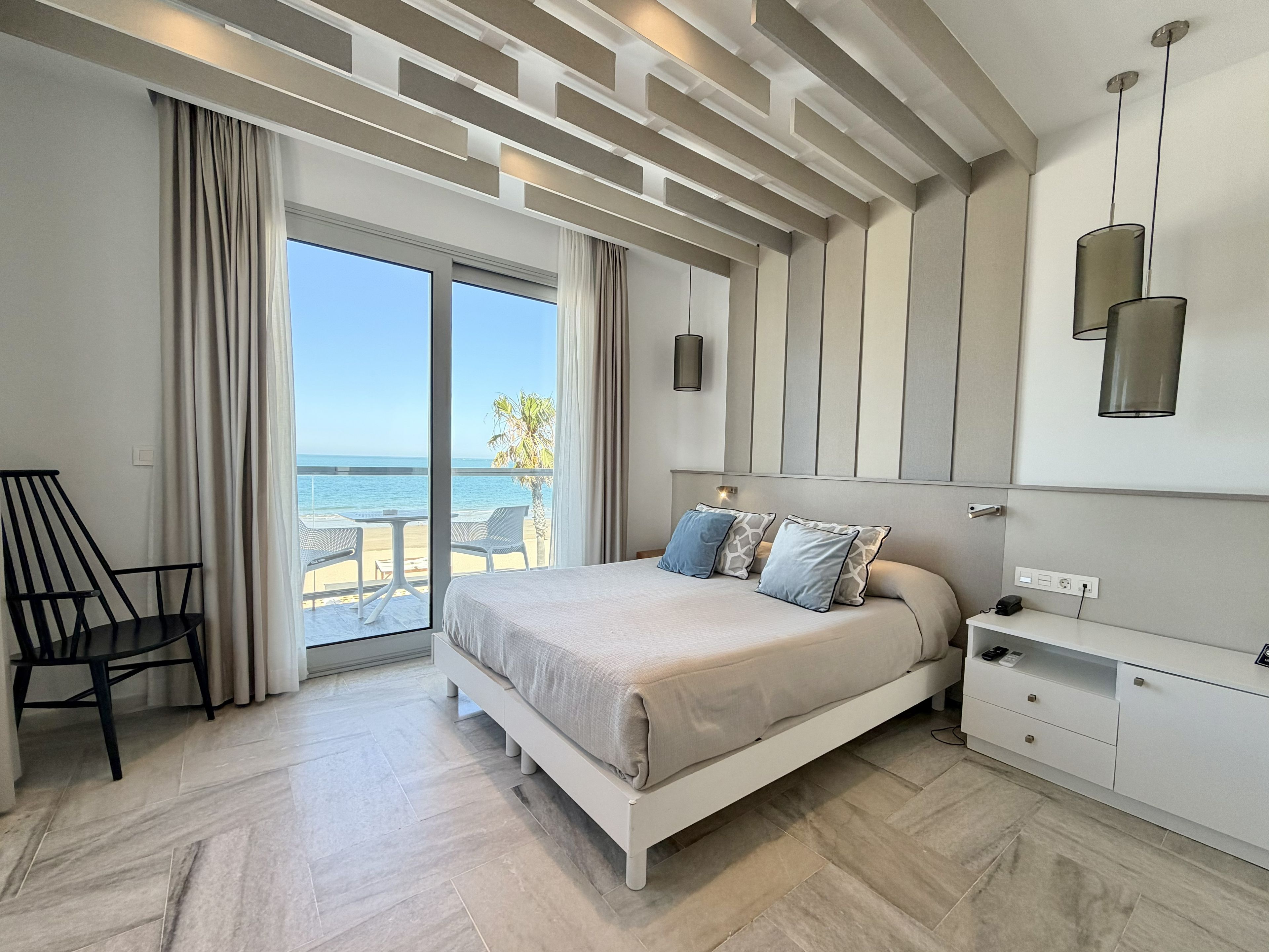 A bedroom with a bed, a desk, and a view of the sea.