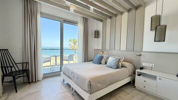 A bedroom with a bed, a desk, and a view of the sea.