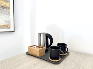 A tray with a stainless steel kettle, two black mugs, and a wooden box on a wooden table against a white wall. - Hotel Apartamentos Marina Luz (Chipiona)
