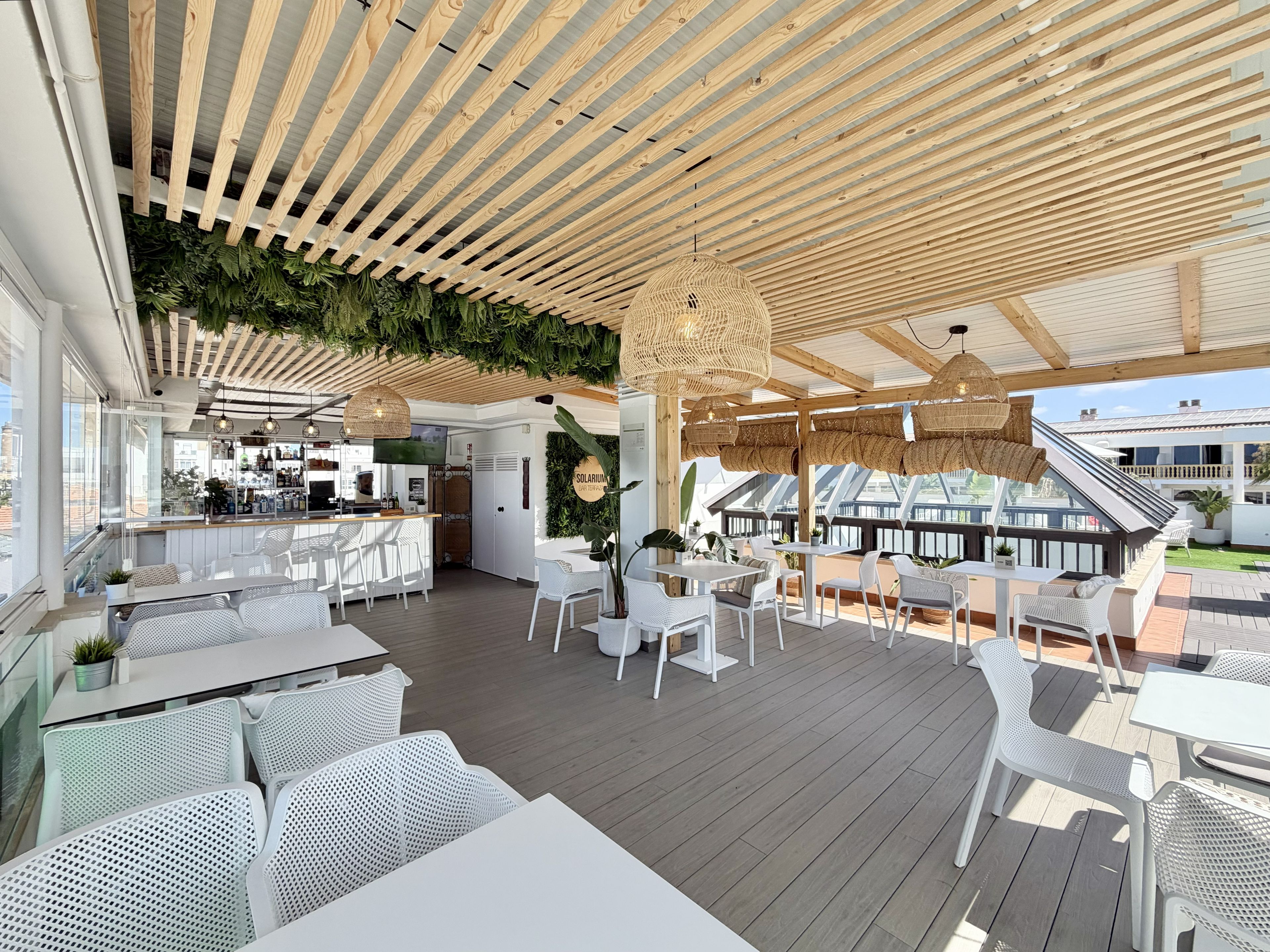 An outdoor dining area with white metal furniture, a bar, and a wooden ceiling with hanging lights.