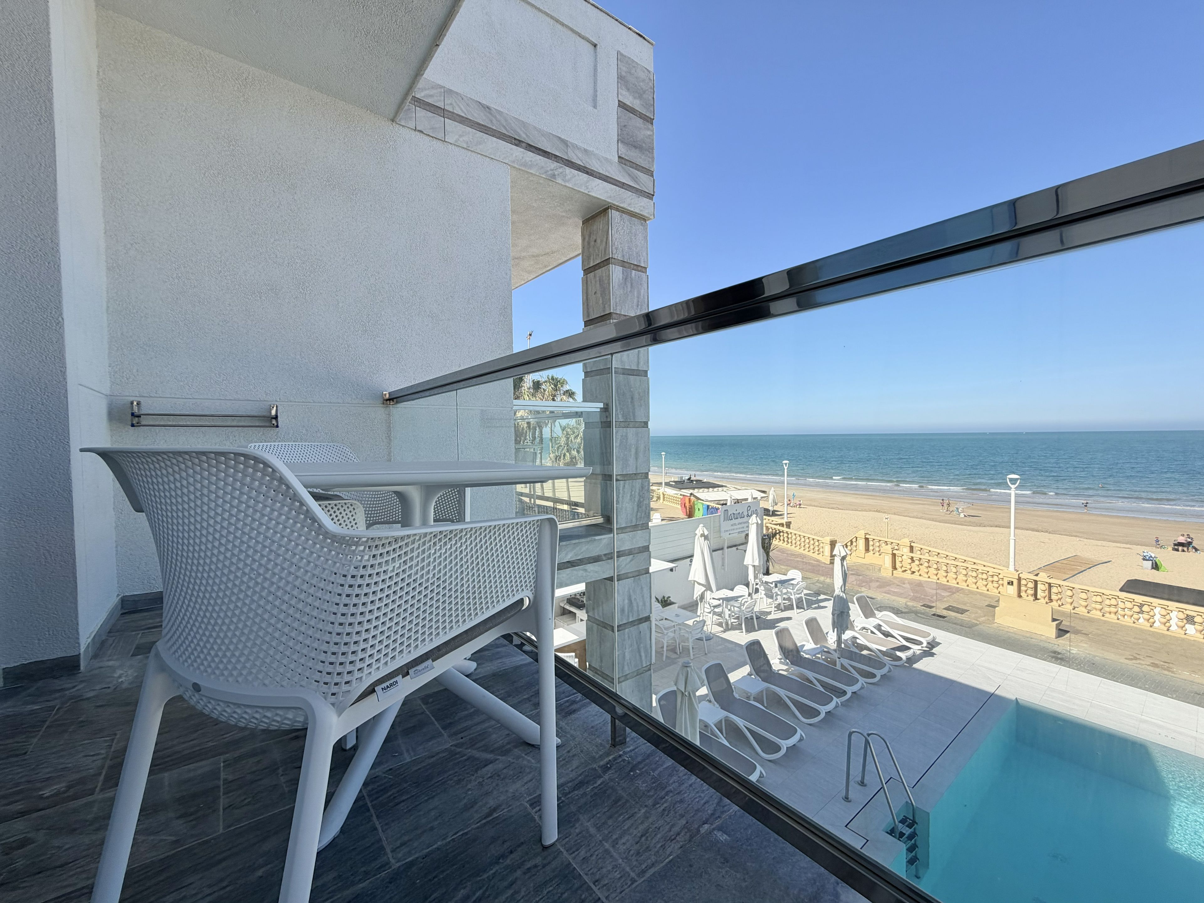 Un balcón con piscina, sillas de descanso y vistas a la playa.