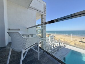 Uma varanda com piscina, cadeiras de sol e vista para a praia.