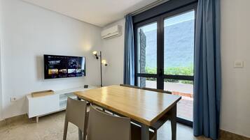 Una habitación con una mesa de madera, dos sillas, un televisor montado en la pared y una ventana con cortinas.