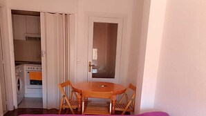 A room with a bed, a green sofa, a wooden table with chairs, and a kitchen area with a washing machine and oven. - Bright and centrally located with views. Wifi and TV. Ski resorts nearby. (Jaca)