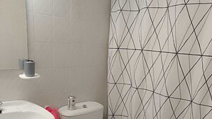 A bathroom with a white sink, toilet, and bidet. There is a trash can and a small mirror above the sink. The walls are tiled with a geometric pattern. - Bright and centrally located with views. Wifi and TV. Ski resorts nearby. (Jaca)