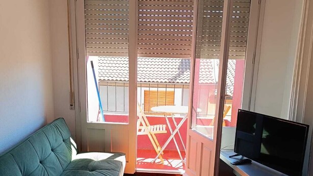 A small room with a green sofa, a TV on a stand, and a sliding door leading to an outdoor area with a table and chairs. - Bright and centrally located with views. Wifi and TV. Ski resorts nearby. (Jaca)