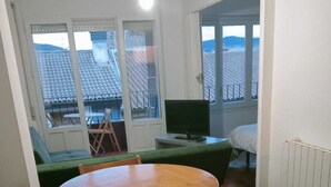 A room with a round wooden table and chairs, a green sofa, a television, and a bed. - Bright and centrally located with views. Wifi and TV. Ski resorts nearby. (Jaca)