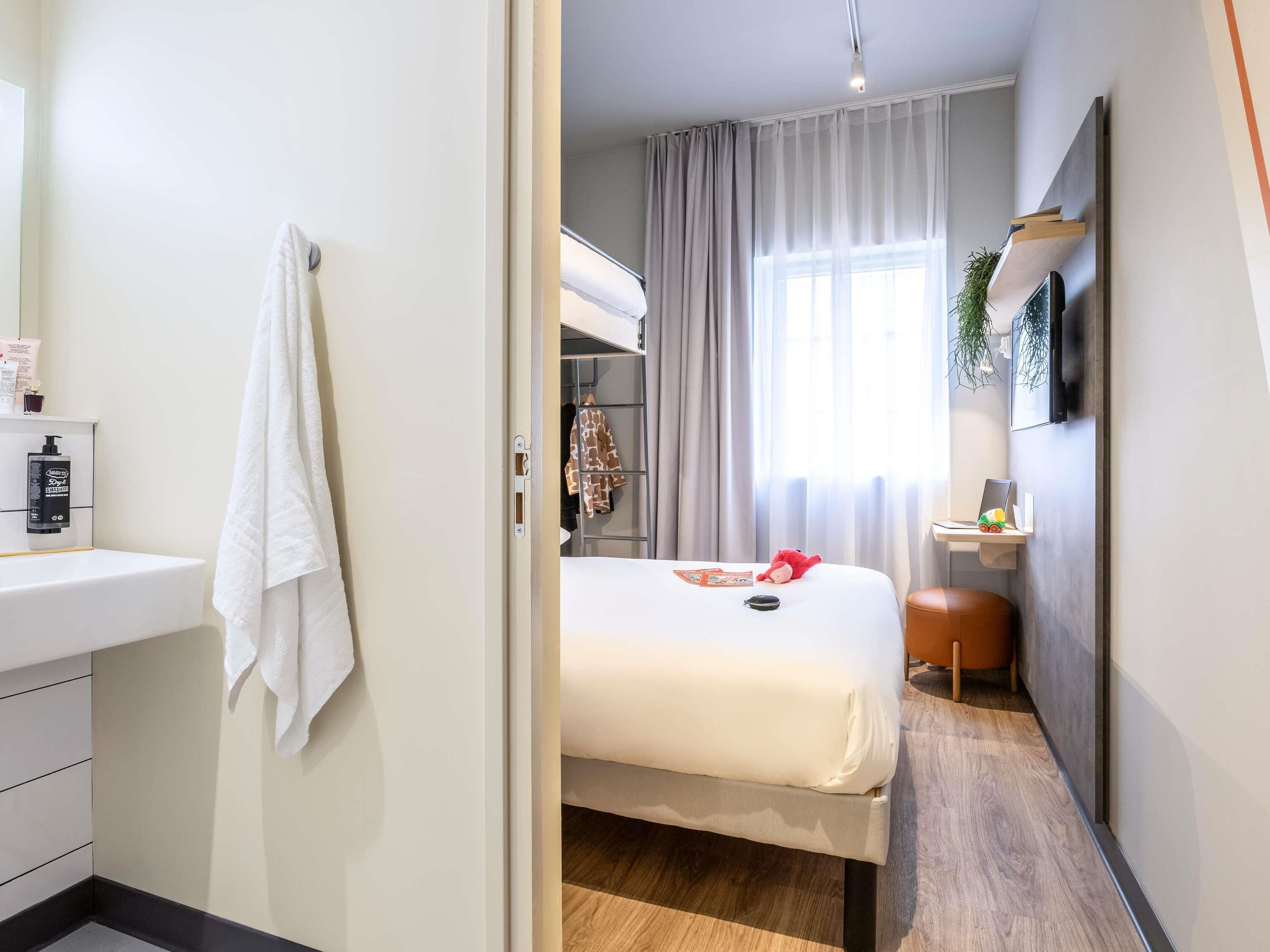 A hotel room with a bed, a desk, a chair, a wardrobe, and a bathroom with a sink and towel.