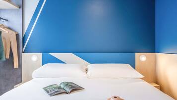 A neatly made bed with white linens, a pink camera, and an open book on the bed.