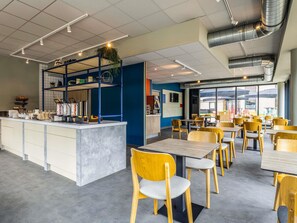 Un café moderno con un mostrador central, zona de estar y amplios ventanales.