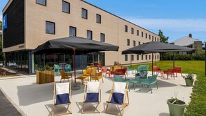A hotel with outdoor seating, a brick facade, and a clear sky. - ibis budget Arlon Porte du Luxembourg (Arlon)