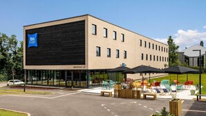 A modern building with a reception area, outdoor seating, and a parking lot. - ibis budget Arlon Porte du Luxembourg (Arlon)