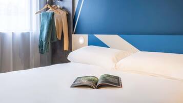 Una habitación de hotel con una cama, un libro, un perchero con ropa y una estantería con objetos.