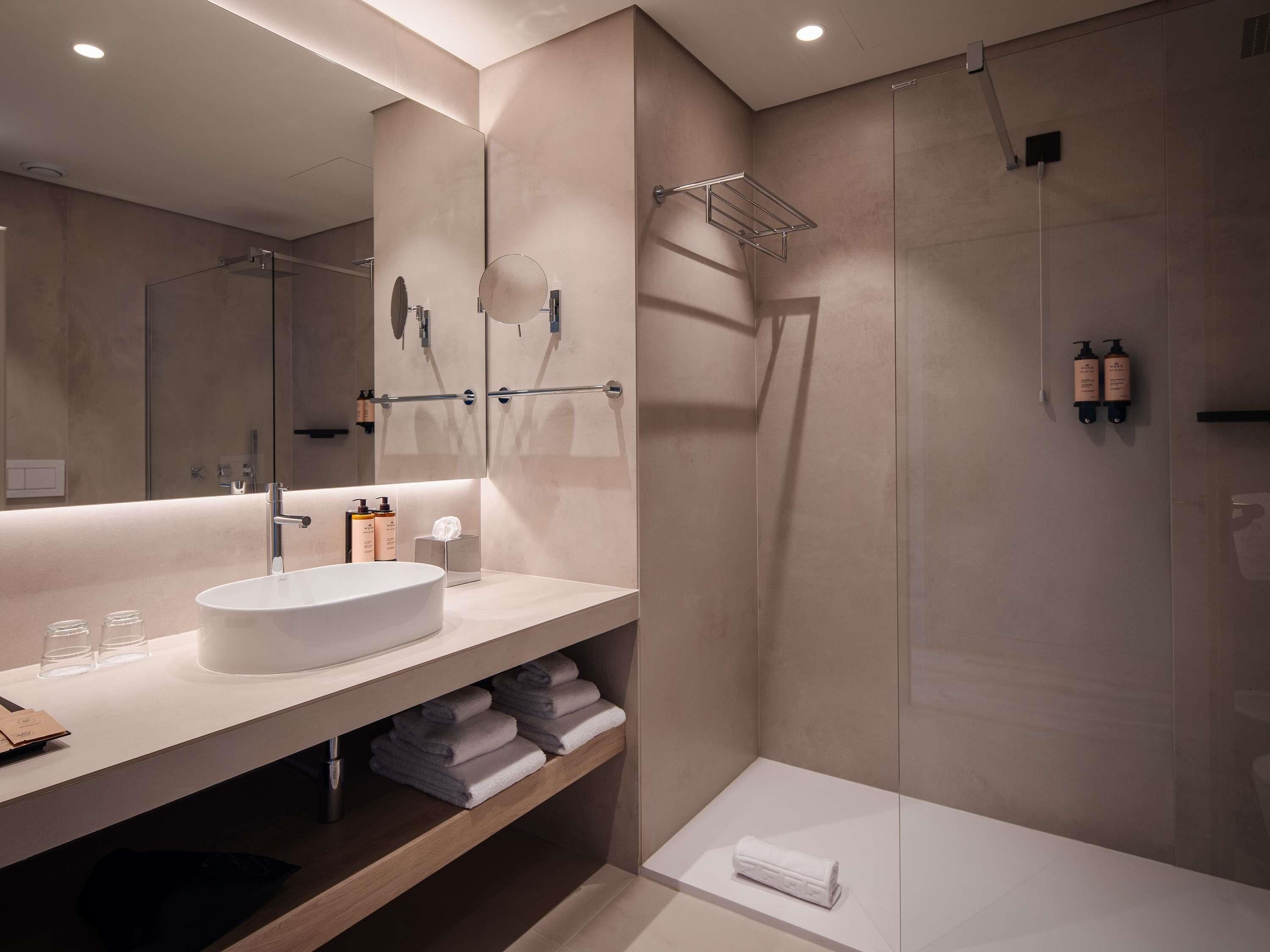 Une salle de bain moderne avec un grand miroir, un lavabo rond et un espace douche.