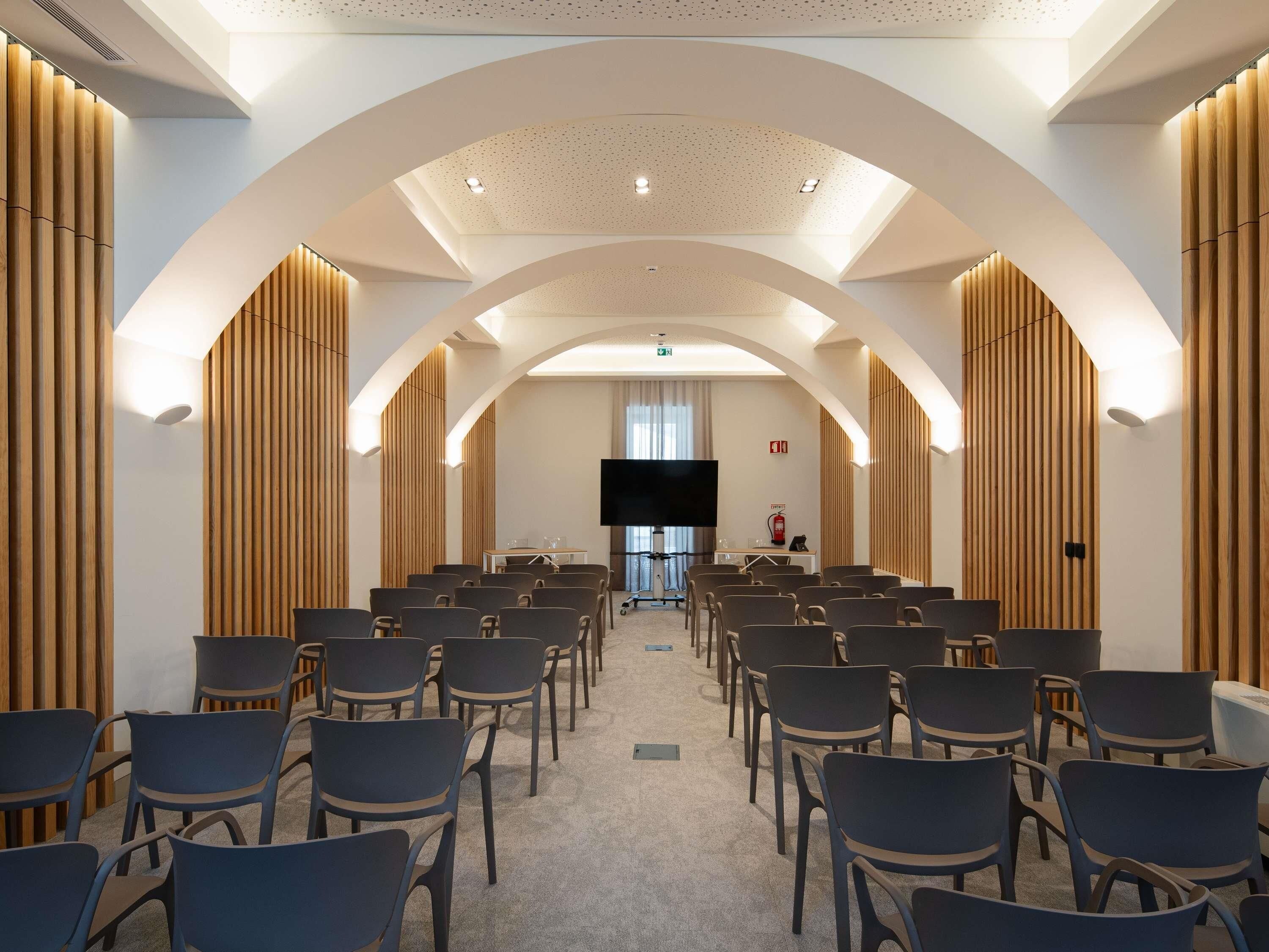 A conference room with rows of chairs, a large screen, and wooden paneling on the walls.