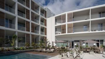 Un hotel moderno con varios balcones, zona de piscina y mobiliario exterior.