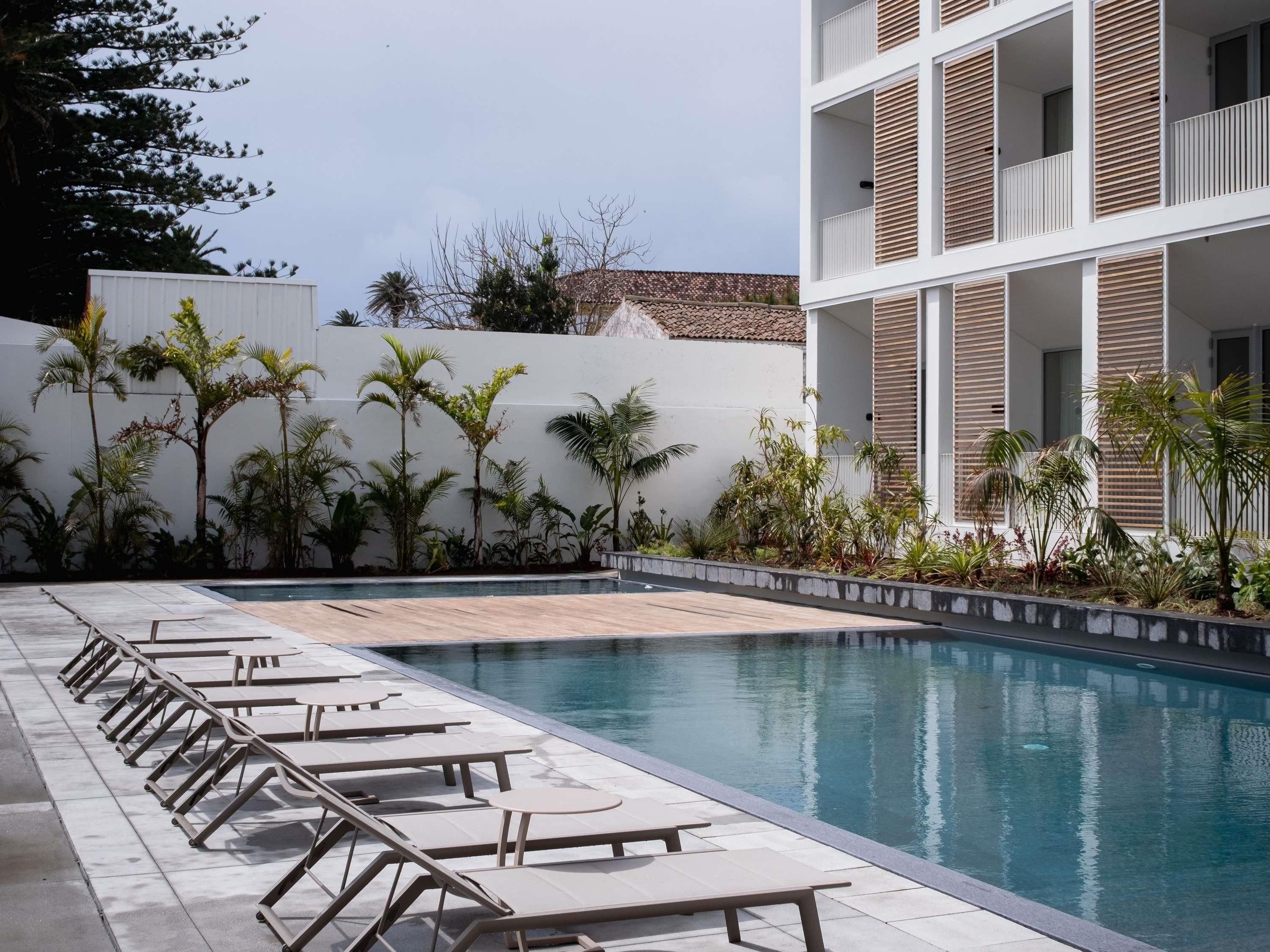 Uma área de piscina com espreguiçadeiras e um edifício com varandas.