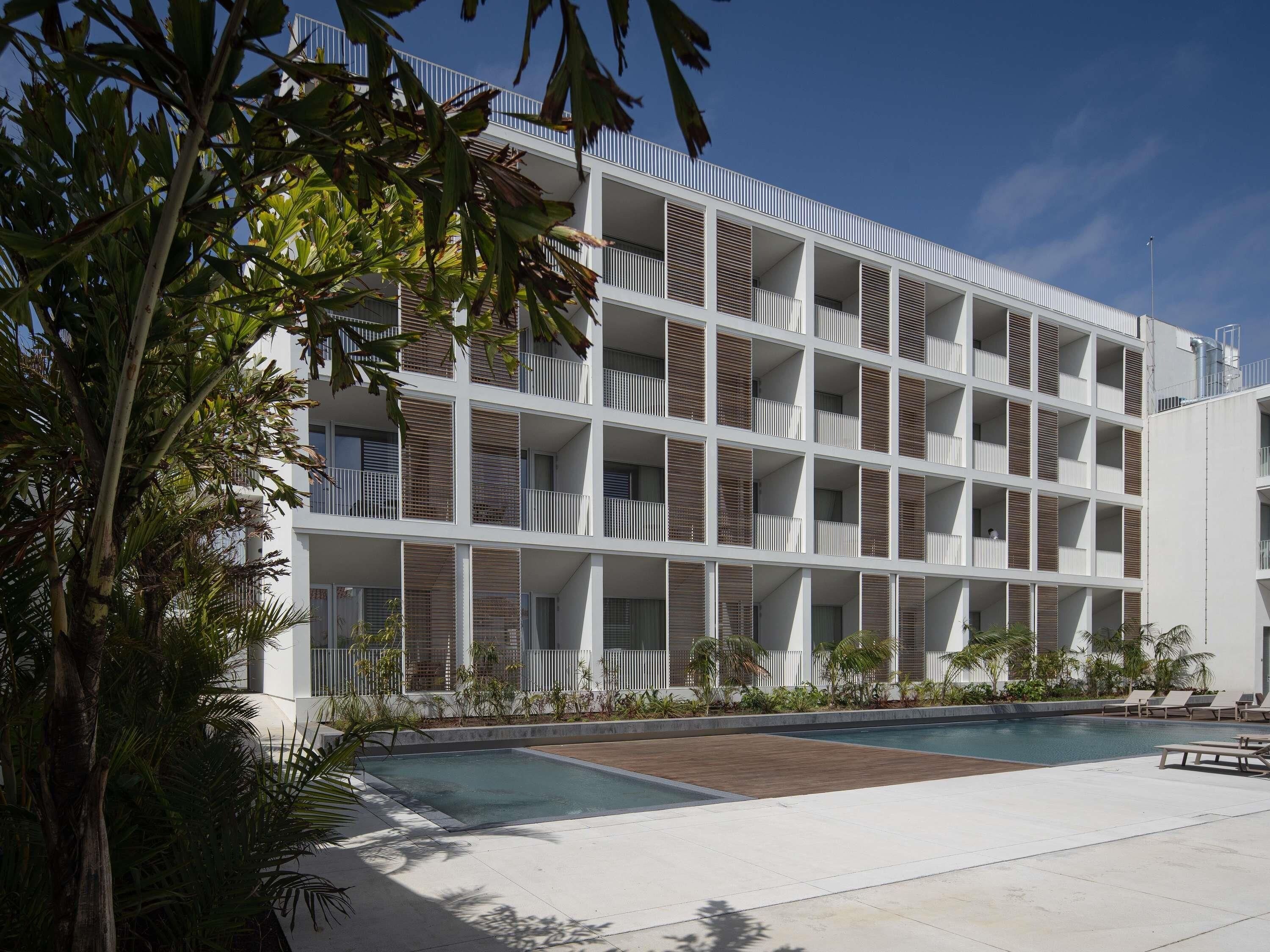 A modern building with multiple balconies, a swimming pool, and tropical landscaping.