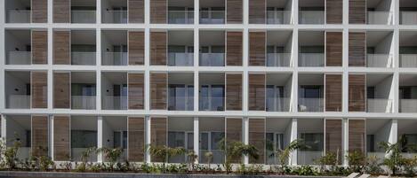 Un hotel moderno de varios pisos con balcones, piscina y sillones de descanso.