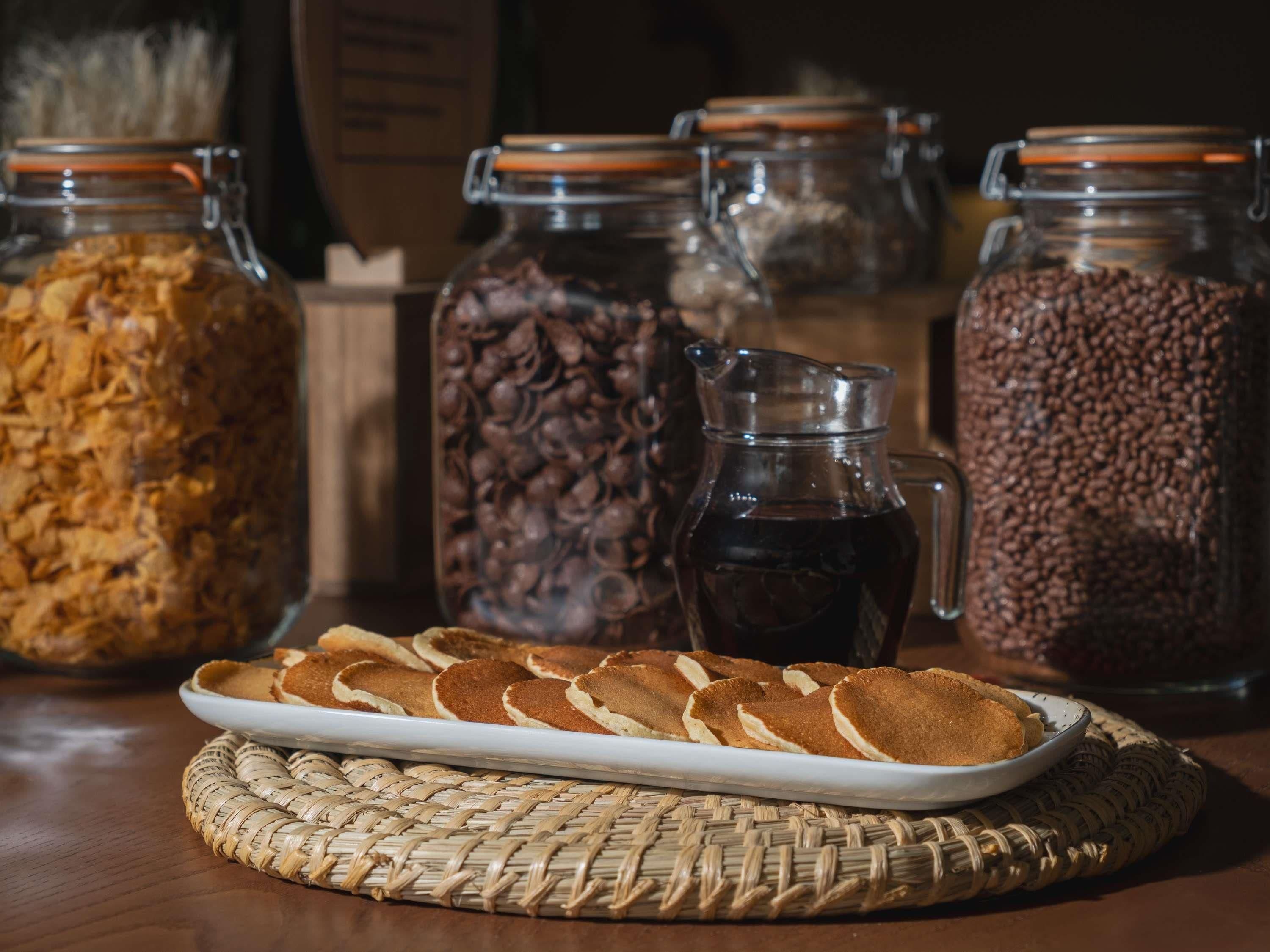 Una mesa con una fuente de tortitas, tarros de granos de café y una jarra de café.