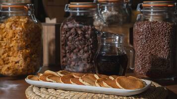 Una mesa con una fuente de tortitas, tarros de granos de café y una jarra de café.
