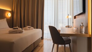 A hotel room with a bed, a desk with a chair, a mirror, and a window with curtains. - Mercure Ponta Delgada Azores (Ponta Delgada)