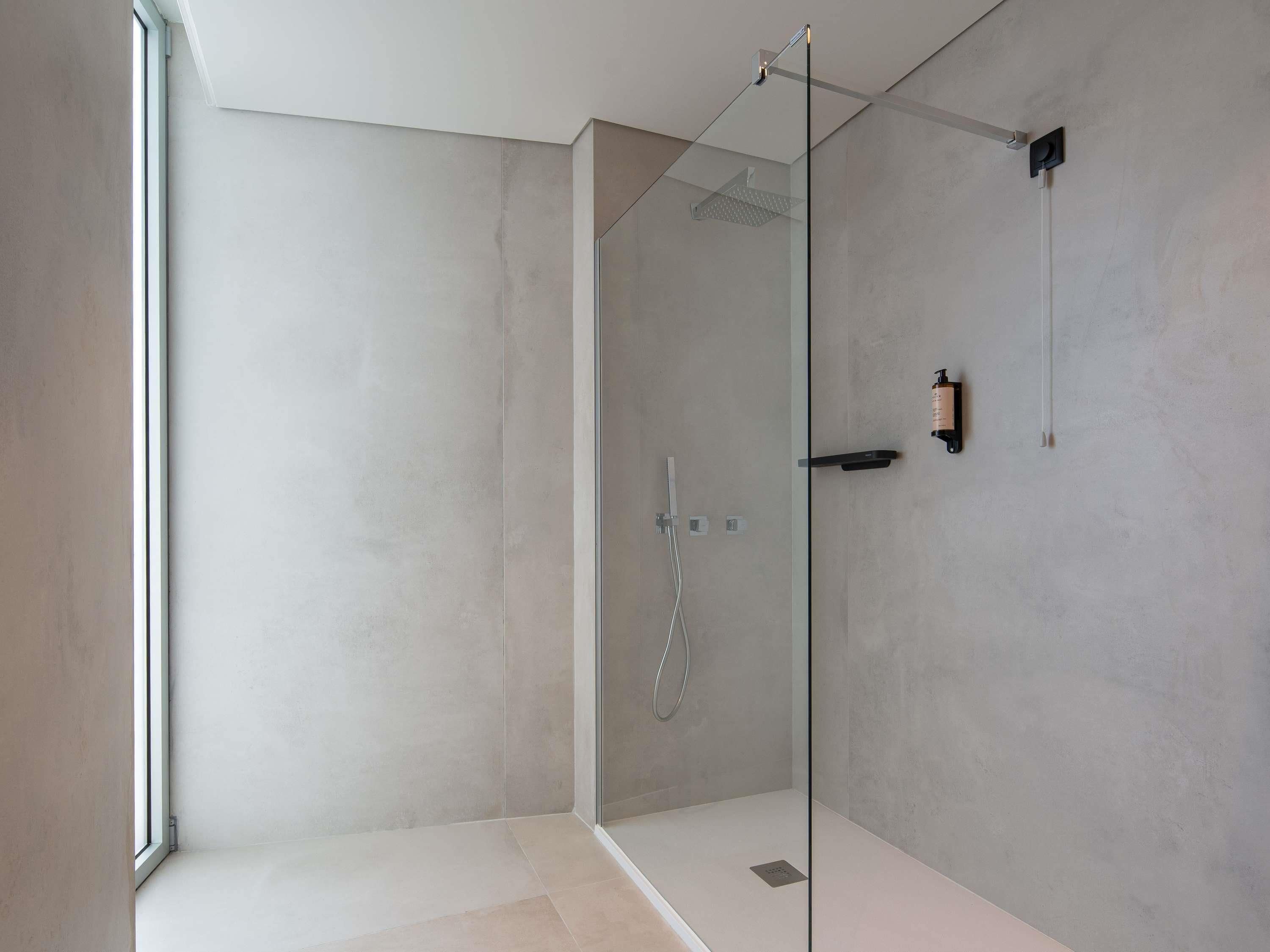A modern shower with a glass door, a handheld showerhead, and a soap dispenser on the wall.