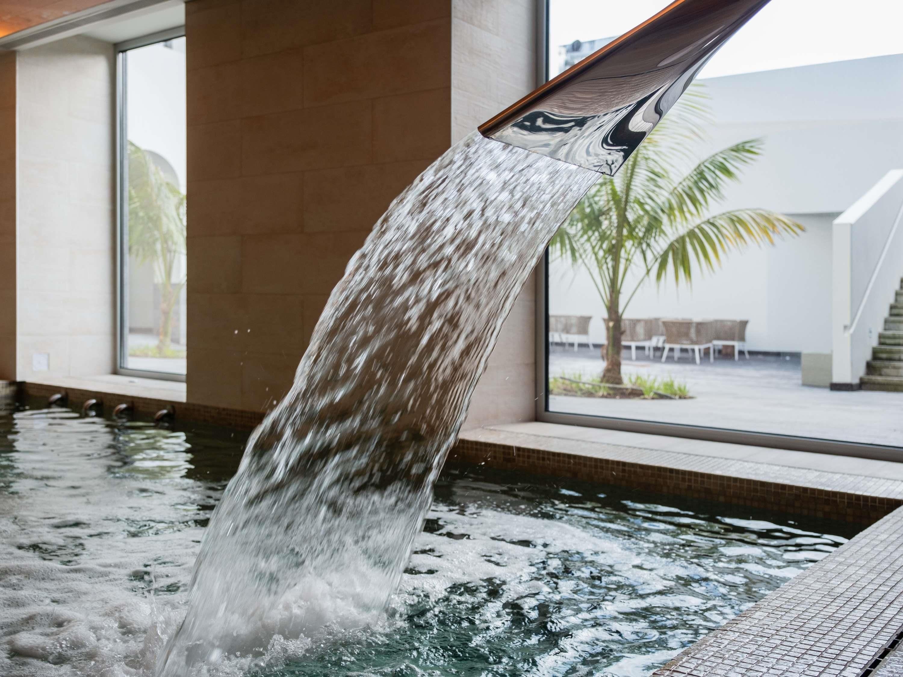 Een waterattractie met een waterval, een zwembad en uitzicht op een terras met palmbomen.