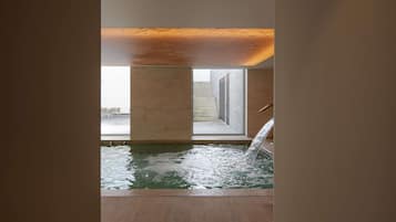 Piscina interior moderna com vista clara para o exterior, piso de madeira e um elemento aquático.