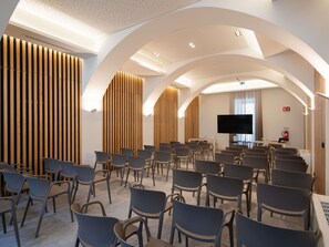 Ein Konferenzraum mit Reihen von Stühlen, einem großen Flachbildfernseher und Holzwandverkleidung.