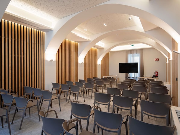 A conference room with rows of chairs, a large flat-screen TV, and wooden panel walls.