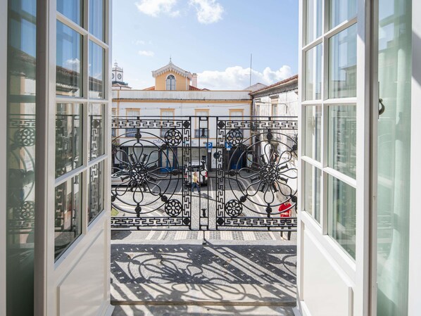 A view through a window with a wrought iron gate, a cobblestone street, and a building with a clock tower in the background. - Mercure Ponta Delgada Azores (Ponta Delgada)