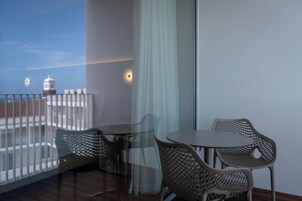 A balcony with wicker chairs and a table, overlooking a building with a clock tower.