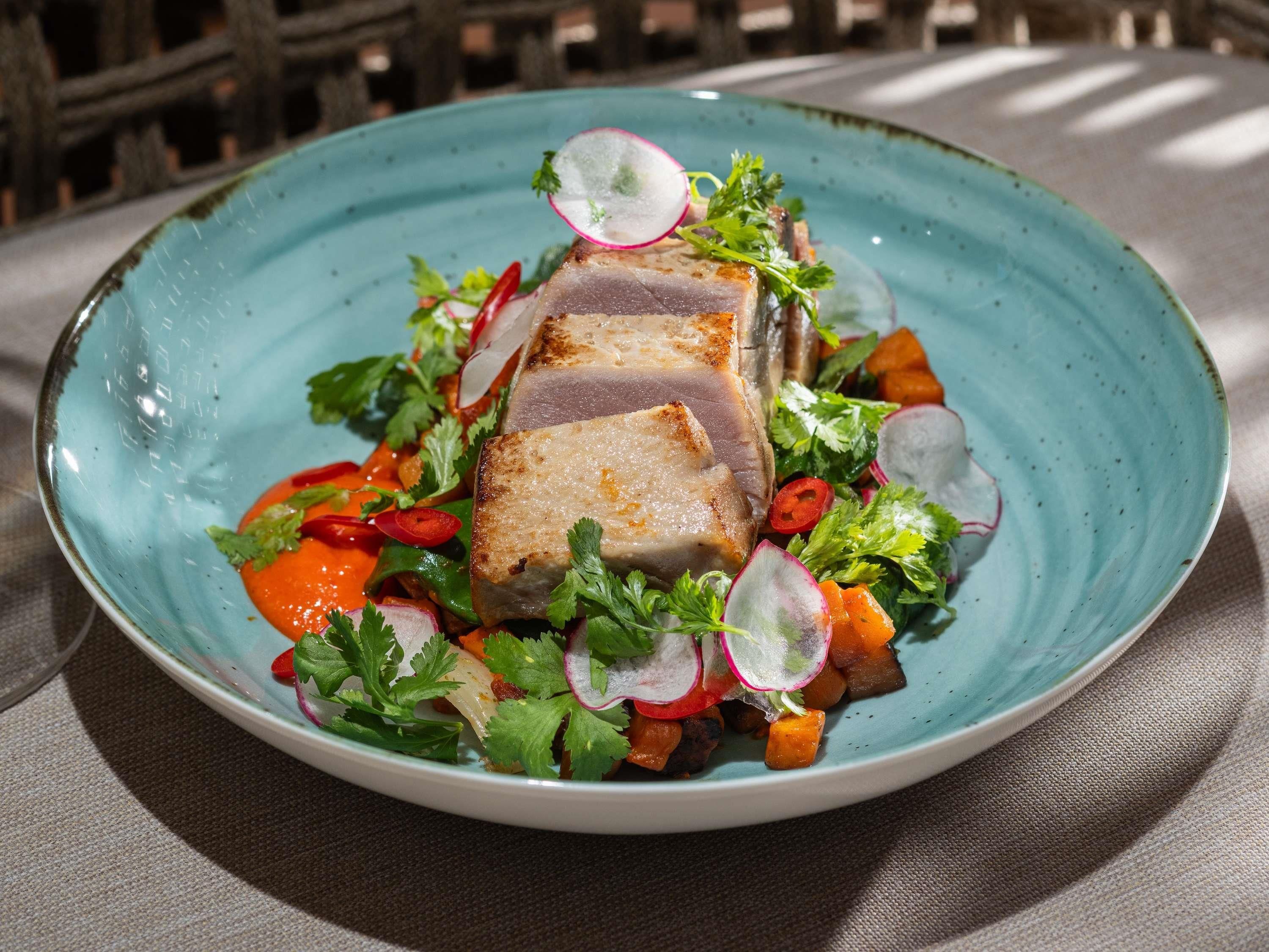 A plate of food with a slice of meat, vegetables, and herbs.