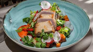 A plate of food with a slice of meat, vegetables, and herbs.