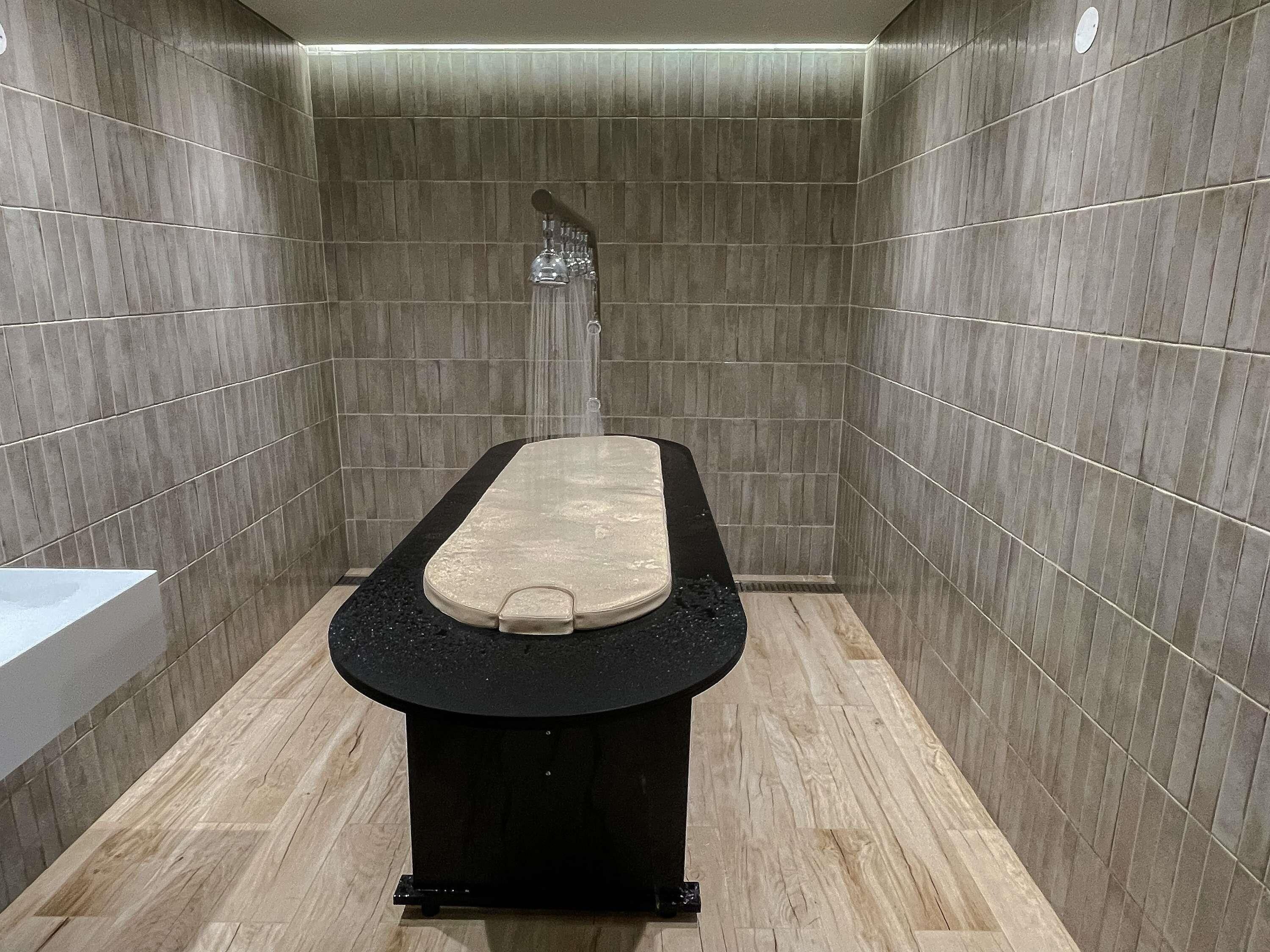 Un baño moderno con una bañera negra, paredes con azulejos y suelo de madera.