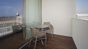 A balcony with a wooden floor, two wicker chairs, a small round table, and a glass partition. - Mercure Ponta Delgada Azores (Ponta Delgada)