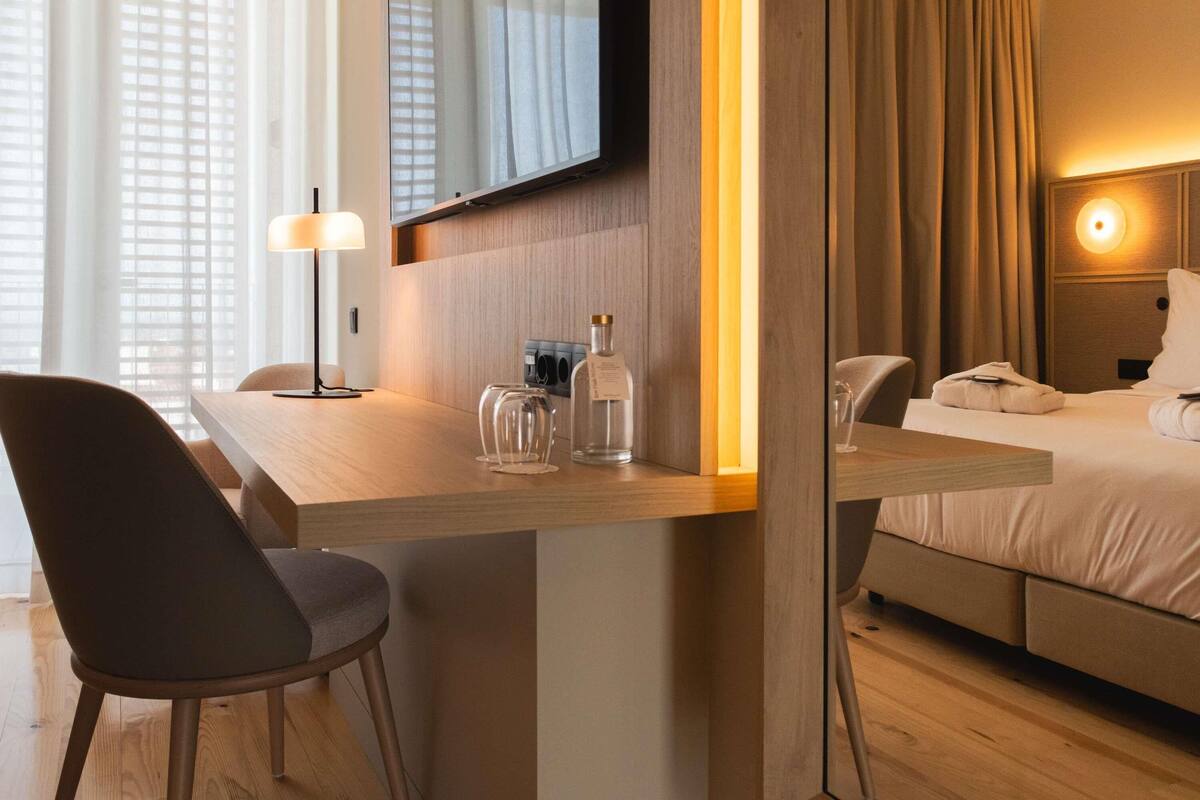 A hotel room with a desk, chair, bed, and a mirror.
