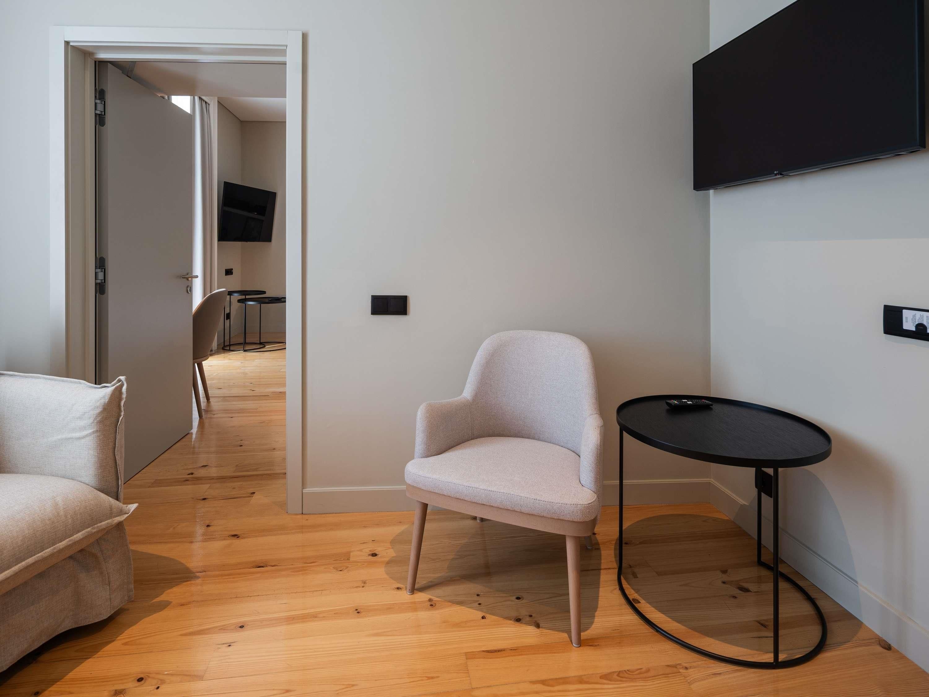 Una habitación moderna con piso de madera, un sillón de color claro, una pequeña mesa redonda y un televisor de pantalla plana montado en la pared.