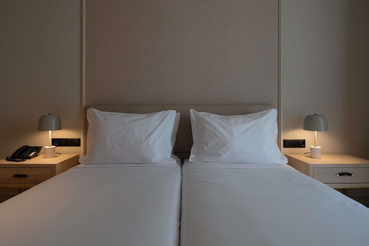 A double bed with white linens, two bedside tables with lamps, a phone, and a wall panel.