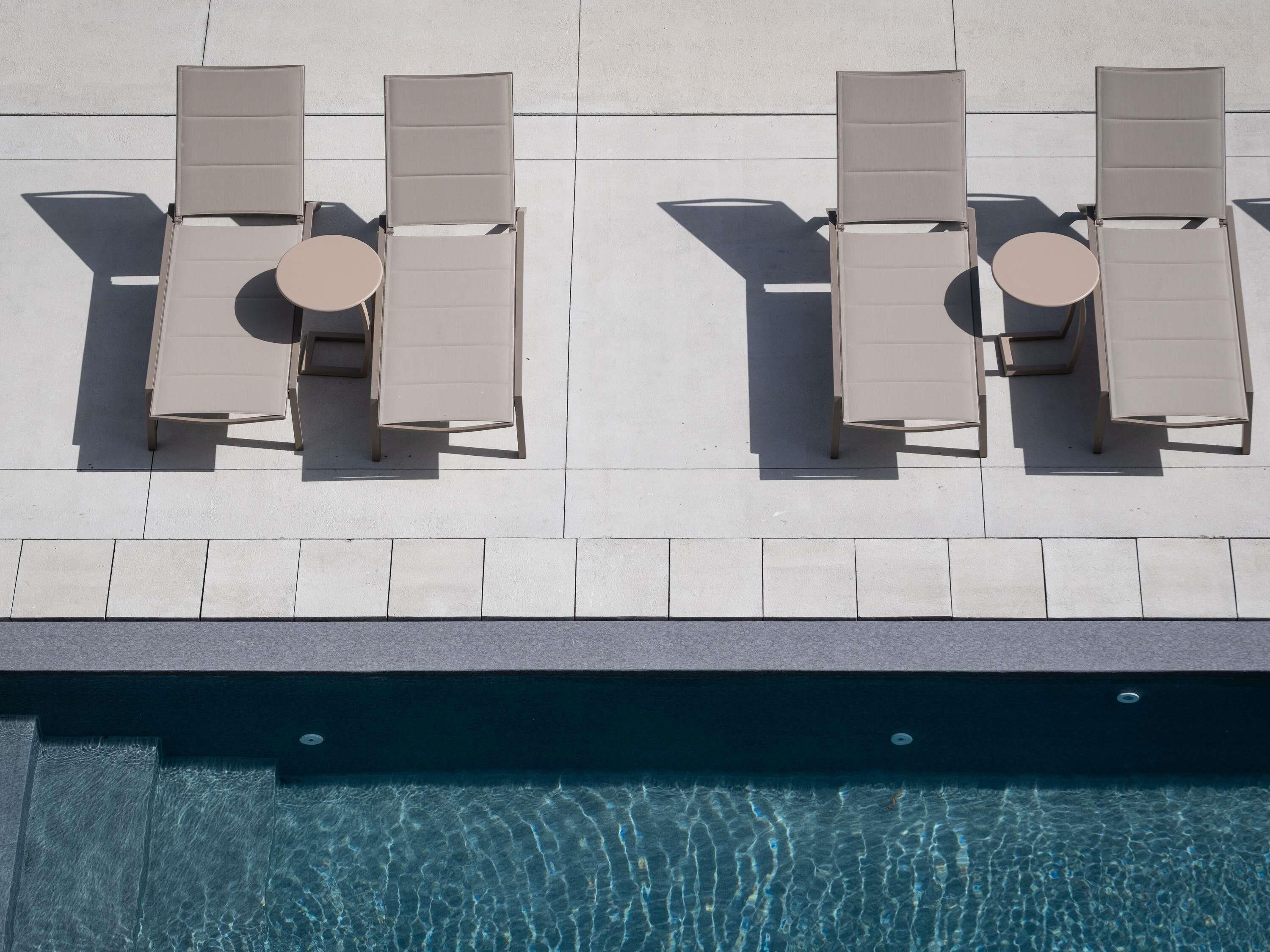 An outdoor seating area with two tables and four chairs, overlooking a swimming pool.