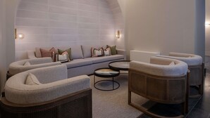 A modern lounge area with a curved sofa, round coffee table, and wicker chairs. - Mercure Ponta Delgada Azores (Ponta Delgada)