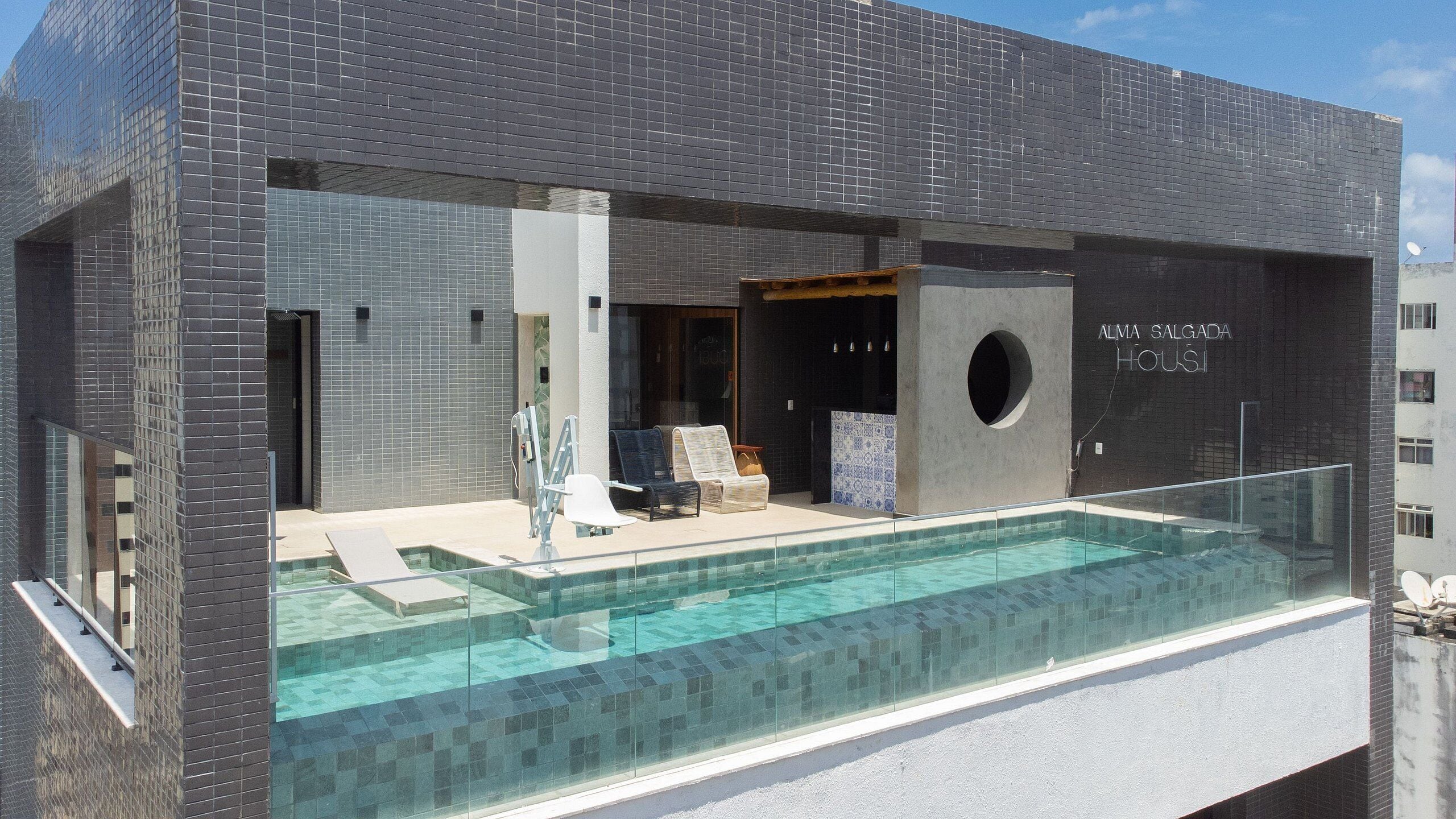 En modern byggnad med en infinitypool som är omgiven av glas, en öppen spis och ett sällskapsrum med fåtöljer.