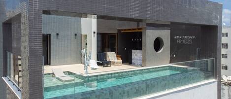 En modern byggnad med en infinitypool som är omgiven av glas, en öppen spis och ett sällskapsrum med fåtöljer.