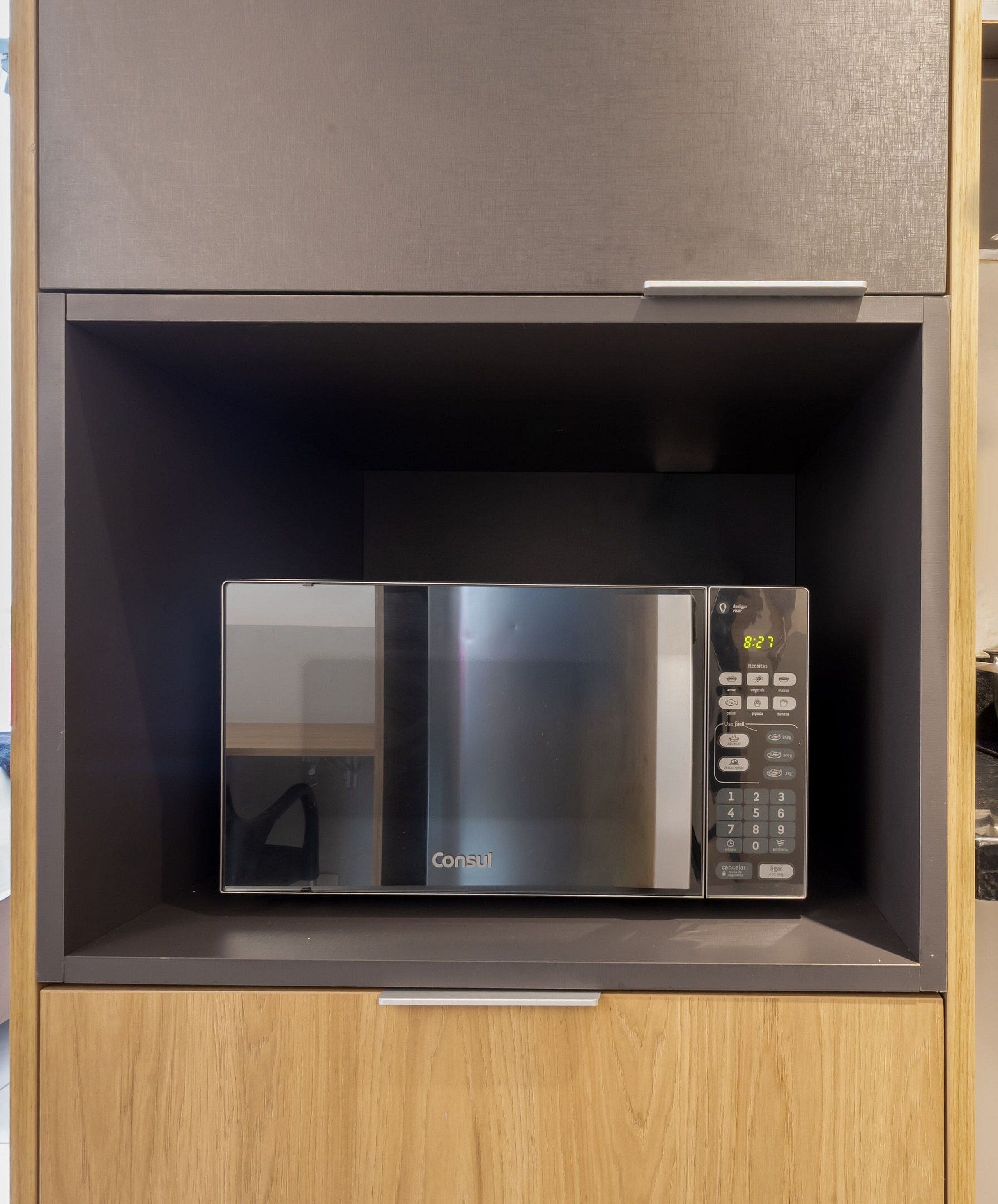Un microondas con pantalla digital y panel de control, dentro de un mueble de madera con un cajón debajo.